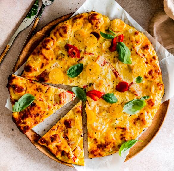 Runde Schüttelpizza angeschnitten auf einem Pizzateller aus Holz getoppt mit frischem Basilikum