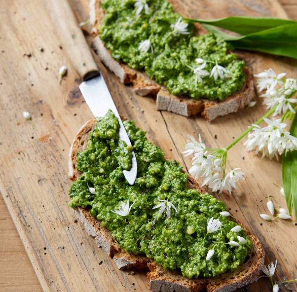 Drei Scheiben Brot mit selbstgemachtem Bärlauchaufstrich auf einem Holzbrett