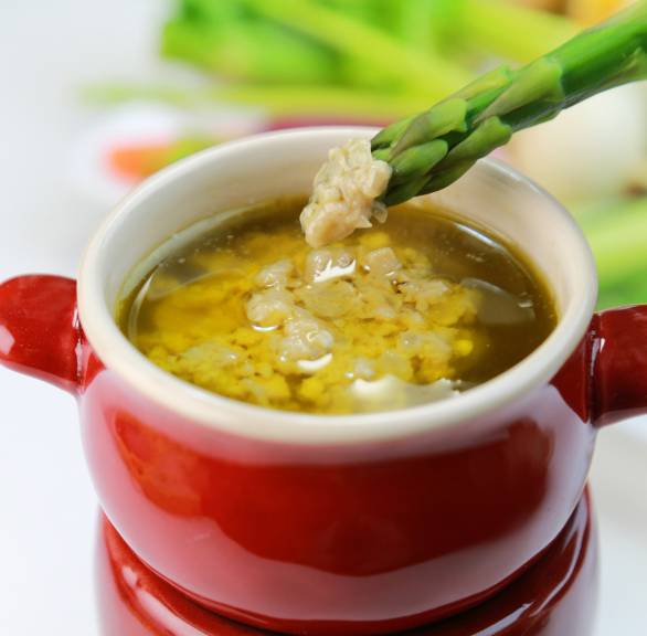 Bagna Cauda Sardellen-Knoblacuh-Sauce in einem Steinguttopf auf einem Stävchen, es wird grüner Spargel hineingedippt