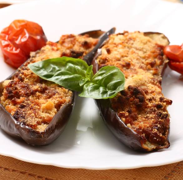 Gefüllte Auberginenhälften aus dem Ofen auf einem Teller dekoriert mit frischem Basilikum