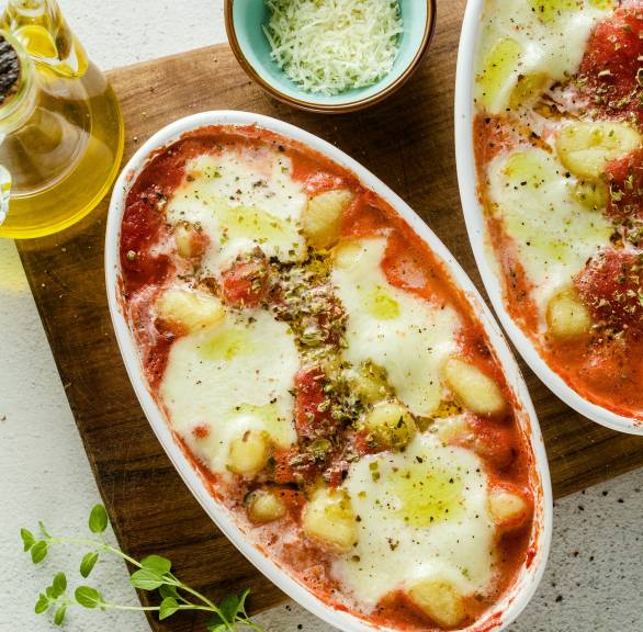 Überbackene Gnocchi alla Sorrentina mit Mozzarella in Tomatensoße in zwei Auflaufformen auf einem Holzbrett