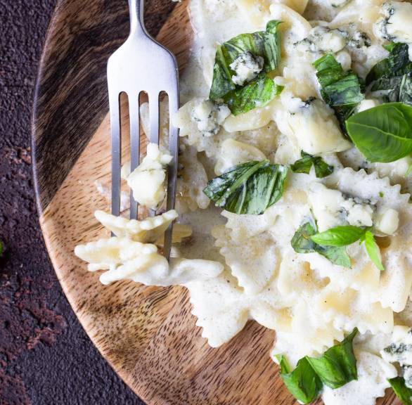 Gorgonzolasauce angerichtet zu Pasta auf einem Holzteller garniert mit frischem Basilikum