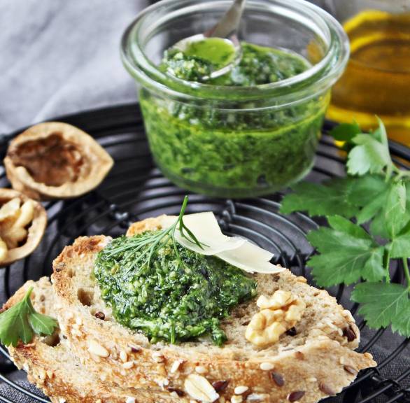 Mangoldpesto auf einem Stück Brot, dahinter ein Glas haltbar gemachtes Pesto