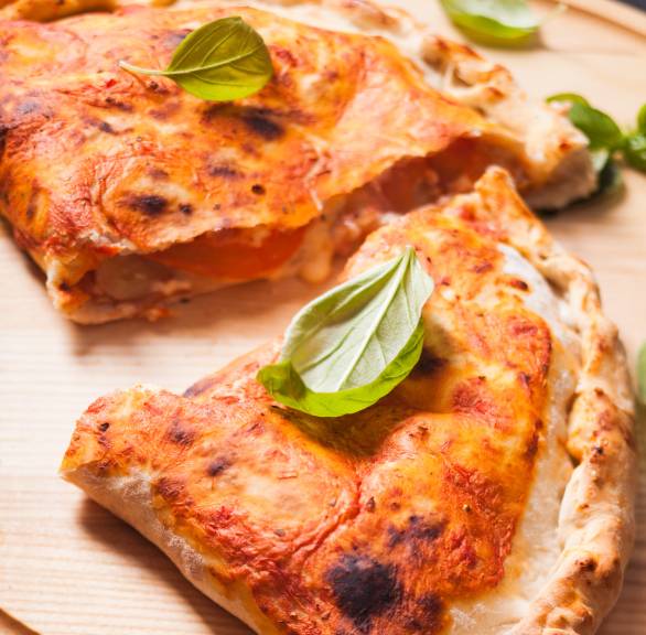 Pizza Calzone halbiert auf einem Holzbrett, Füllung mit Käse gut sichtbar