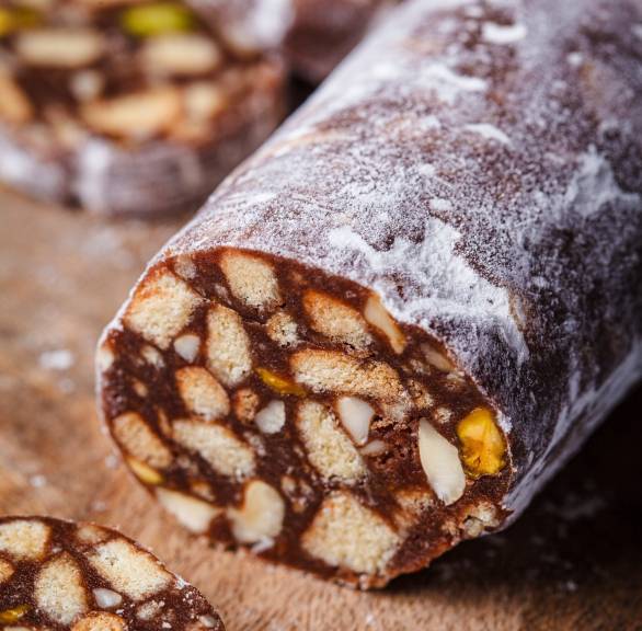 Selbst gemachte Schokosalami mit Keksen und Nüssen angeschnitten auf einem Holzbrett