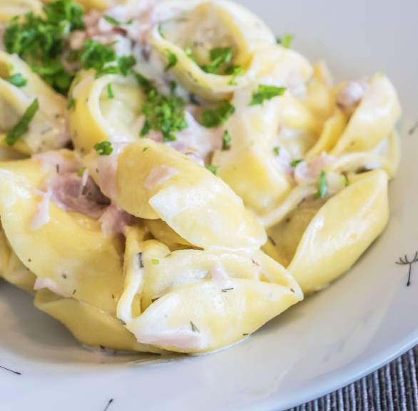 Tortellini alla panna mit Schinken-Sahne-Soße auf einem tiefen Teller im close up
