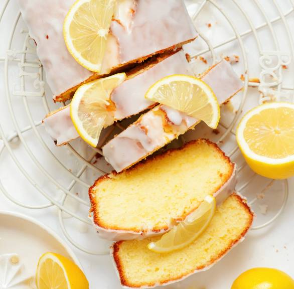 Zitronenkuchen mit Olivenöl aus der Kastenform angeschnitten auf einem Kuchengitter, daneben Zitronen