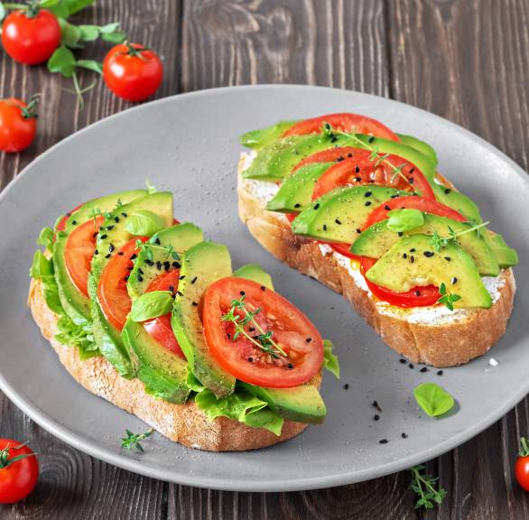 Zwei Avocado-Bruschettas mit Tomaten, veganem Frischkäse und Salat auf einem Teller