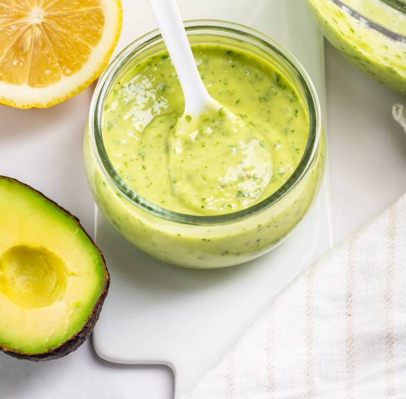 Selbst gemachtes Avocado-Pesto in einem Schälchen, daneben eine halbierte Avocado und eine Zitrone