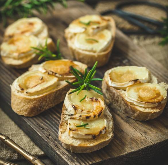 Fünf Bruschettas mit geschmolzenen Ziegenkäsetalern getoppt mit Honig und Rosmarin auf einem Holzbrett