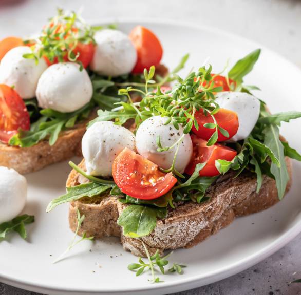 Zwei Bruschettas belegt mit Tomate, Mozzarella und Rucola auf einem Teller
