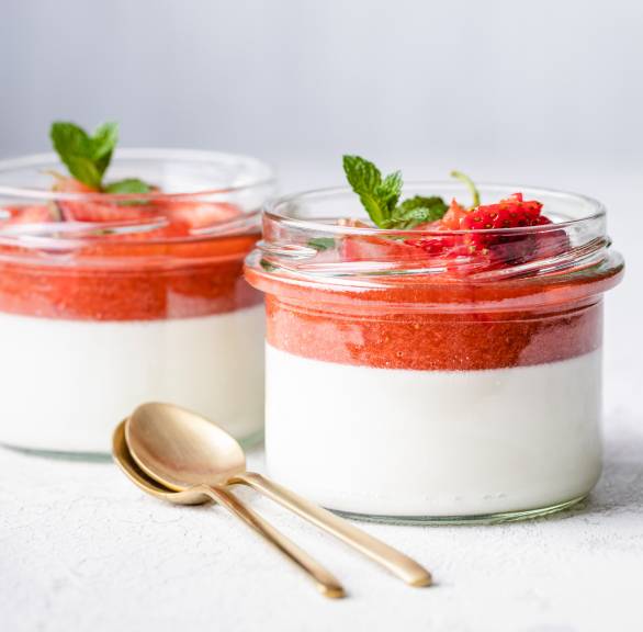 Erdbeer-Panna Cotta geschichtet in zwei Gläser getoppt mit Erdbeerspiegel und Minze auf einem Tisch