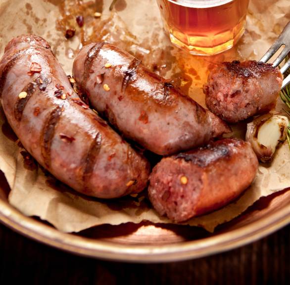 Gegrillte Salsiccia auf einem Tonteller, daneben Knoblauch und Rosmarin
