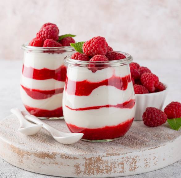 Joghurt-Panna cotta in zwei Gläsern geschichtet mit frischer Himbeersoße, getoppt von Beeren und Minze