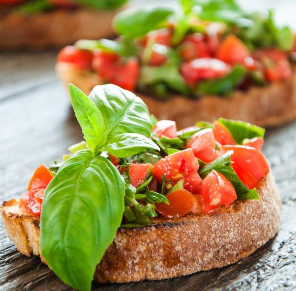 Drei Bruschetta mit frischen Tomaten und Basilikum auf einer Holzplatte