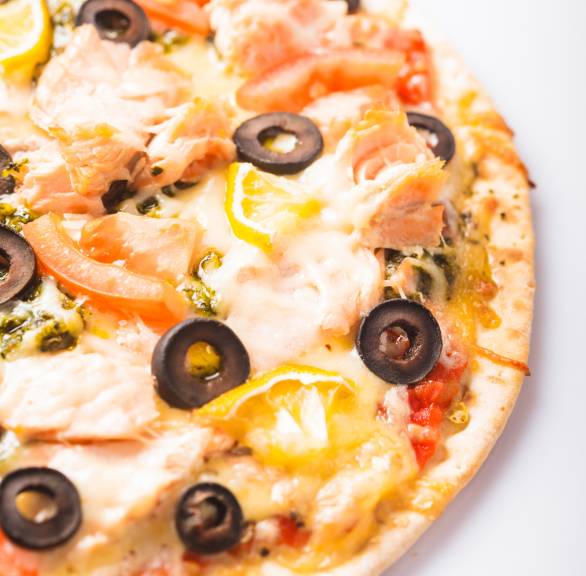 Runde Lachs-Pizza mit Zitrone, Tomaten, Oliven und Mozzarella angeschnitten auf einem Teller