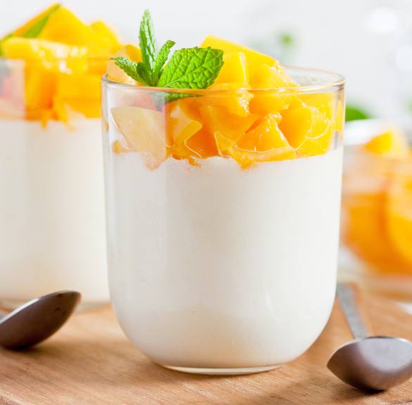Mango-Panna cotta in zwei Gläsern getoppt von frischer Minze auf einem Tisch