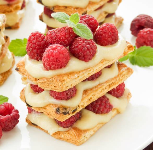 Millefoglie-Torte aus Blätterteigschichten gefüllt mit Vanillepudding-Creme und frischen Himbeeren auf einem Tisch