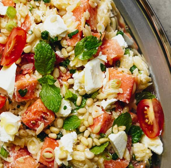 Orzo-Salat mit Feta und Wassermelone auf einem ovalen Teller getoppt von Pinienkernen und frischer Minze