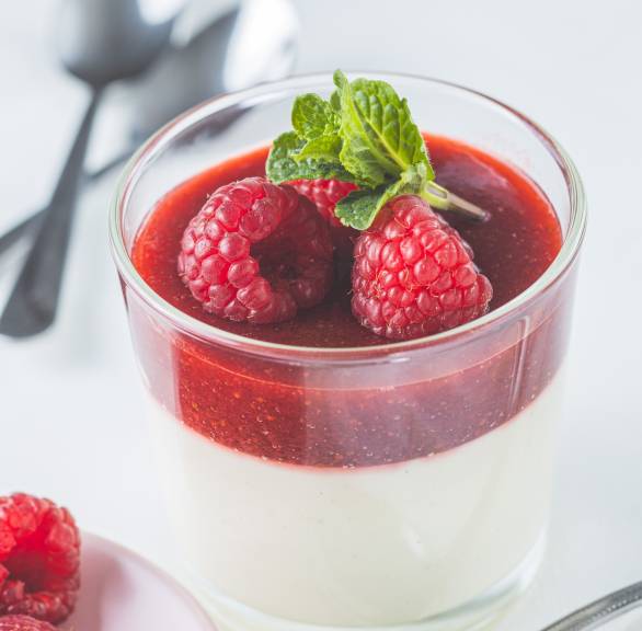 Panna cotta in Dessertgläsern getoppt von Himbeersoße und Minzblättern auf einem Tisch