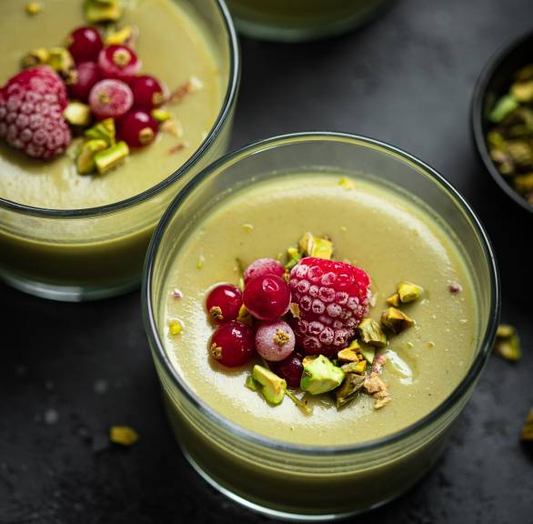 Pistazien-Panna Cotta in drei Gläsern getoppt von Pistazienkernen und Beeren auf einem Tisch von oben