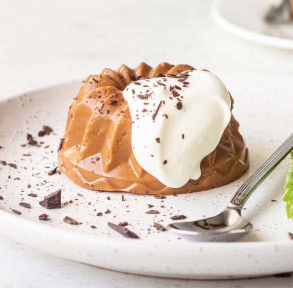 Selbst gemachtes Schoko-Panna Cotta auf einem Dessertteller getoppt von Sahne und Minzblättern