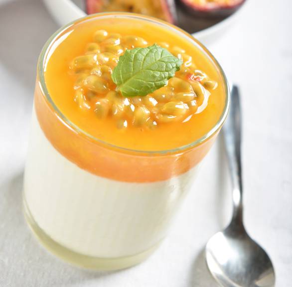 Solero-Panna cotta in einem Glas, daneben halbierte Maracujas auf einem Tisch