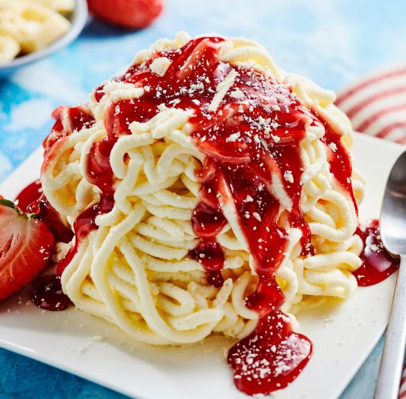 Selbst gemachtes Spagehttieis getoppt mit Erdbeersoße und weißen Schokoladenraspeln auf einem Dessertteller