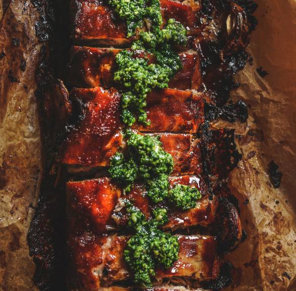 Ein Rack marinierte, gebackene Spareribs auf einem Backblech getoppt von grünem Pesto