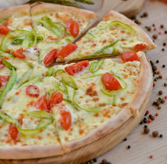 Spargelpizza mit weißem und grünem Spargel, Kirschtomaten Crème fraîche bestrichen angeschnitten auf einem Pizzabrett