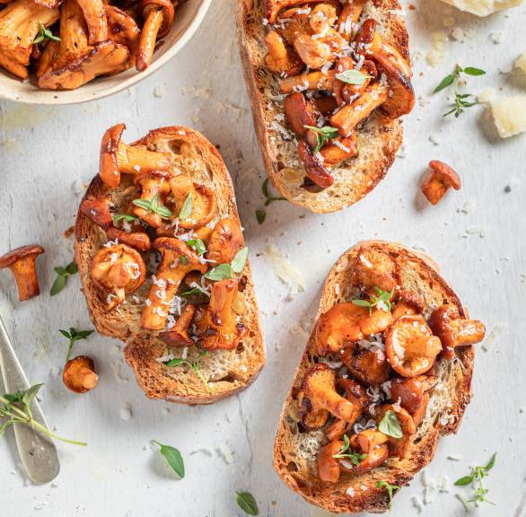 Drei Steinpilz-Bruschette auf einem Teller, daneben eine Schale mit Gebratenen Pilzen und Olivenöl auf einem Tisch