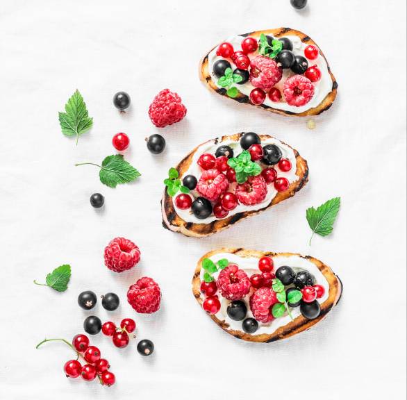 Drei süße Bruschettas getoppt mit Ricotta, Honig, Beeren und Minze auf einem Tisch