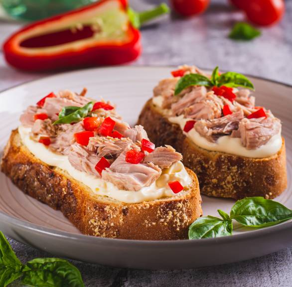 Zwei Thunfisch-Bruschette mkt Frischkäse, Paprika und Tomaten garniert mit Basilikumblättern auf einem Teller