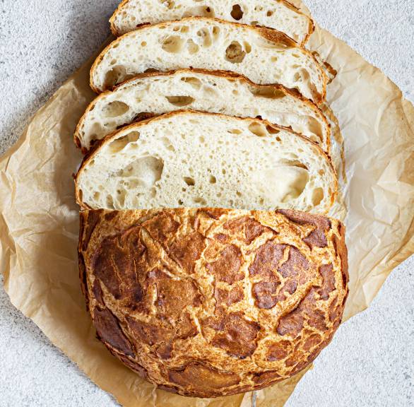 Ein angeschnittener Laib Tigerbrot mit rissiger Kruste auf einem Stück Backpapier