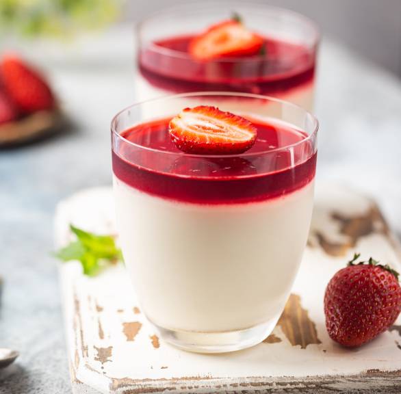 Vegane panna cotta in zwei Gläsern mit Erdbeerspiegel und Minze getoppt auf einem Holzbrett