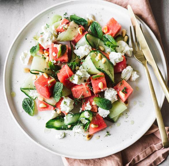 Wassermelonen-Feta-Salat mit Gurke auf einem Teller getoppt von Minzblättern und Pinienkernen