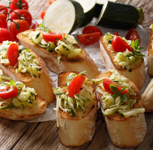 Sechs vegane Zucchini-Bruschettas mit Tomaten auf einem Holztsich