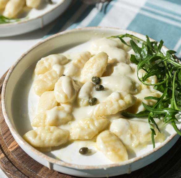 Gnocchi mit Asiago-Käsesoße auf einem Teller angerichtet mit Rucola und garniert mit Kapern