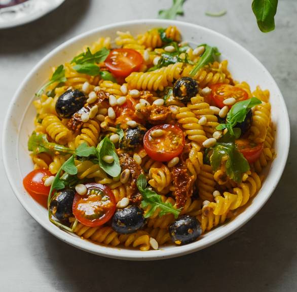 Italienischer Nudelsalat mit Pesto, getrockneten und frischen Tomaten, Oliven und Rucola auf einem Teller