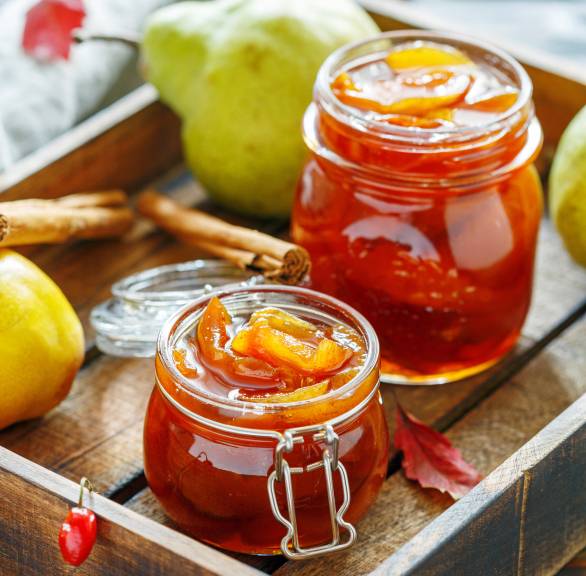 Selbst gekochte Birnenkonfitüre in zwei Weckgläsern auf einem Holztablett, daneben Zimtstangen auf einem Tisch