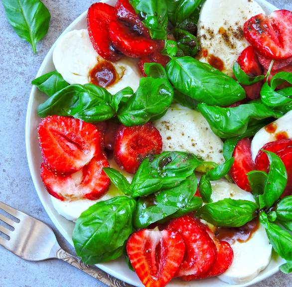 Erdbeer-Caprese angerichtet auf einem Teller mit Mozzarellascheiben und Basilikum, daneben Olivenöl