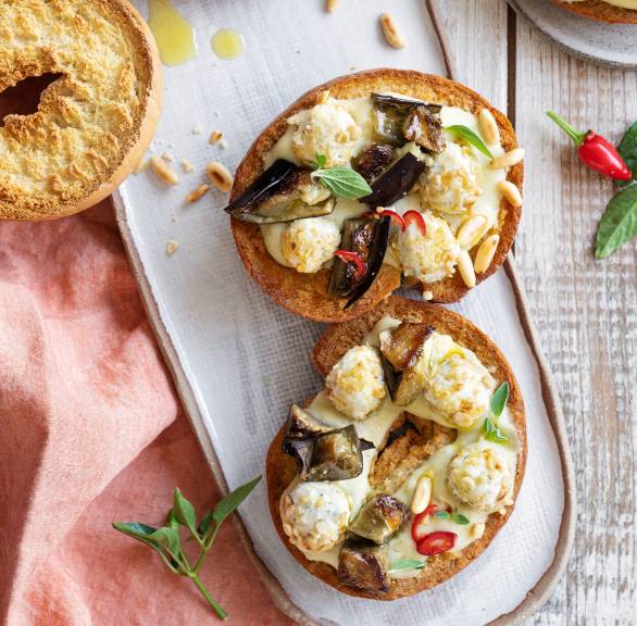 Mehrere Brotringe bestrichen mit Auberginencreme und getoppt von Pinienkern-Käsebällchen auf einer Servierplatte