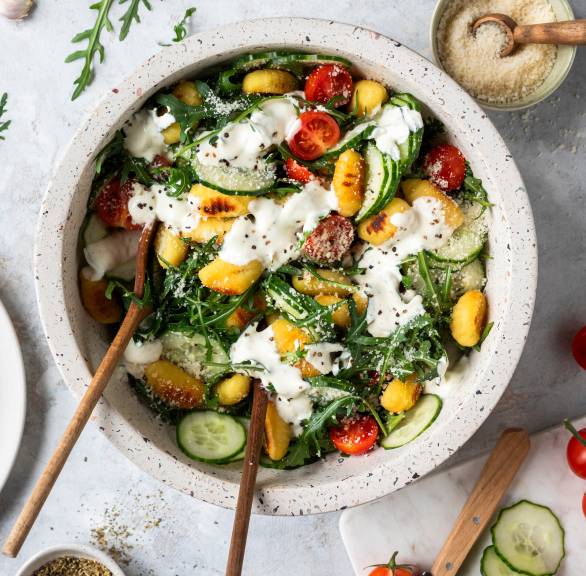 Gurkensalat mit gebratenen Gnocchi in einer Salatschüssel, daneben Zutaten und Parmesan