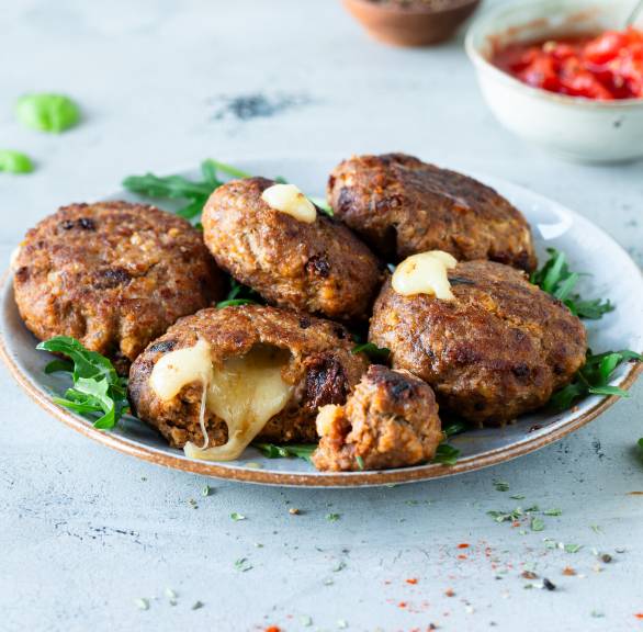 Gefüllte Frikadellen auf einem Teller, teilweise durchgeschnitten mit herauslaufendem, geschmolzenem Mozzarella