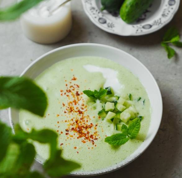 Kalte Gurkensuppe in einem Suppenteller getoppt von Joghurt und Gurkenstücken sowie Gewürzen