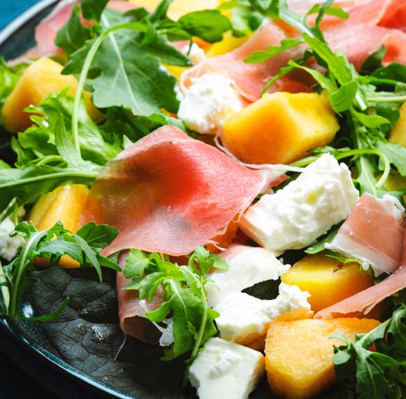 Melonensalat mit Rucola, Prosciutto und Mozzarella in einem tiefen Teller in Nahaufnahme auf einem Tisch