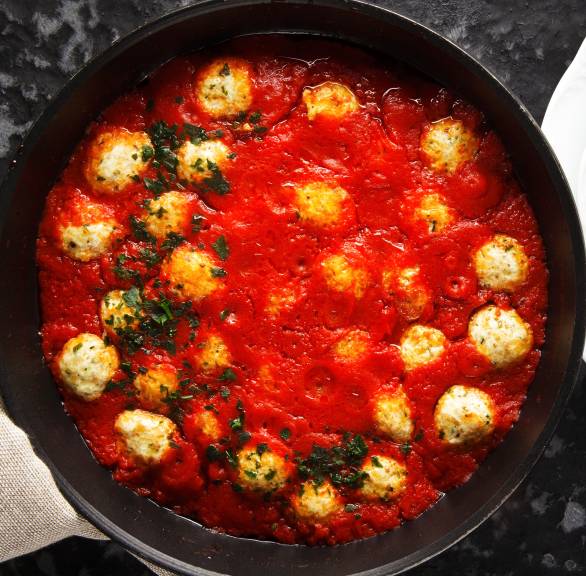 Ricotta-Bällchen in Tomatensoße in einem Topf getoppt mit Basilikum auf einem Esstisch