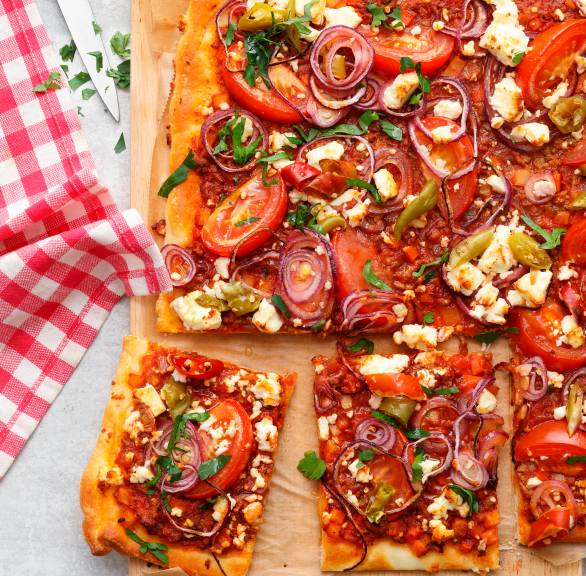 Pizza vom Blech belegt mit Paprika, Tomaten und Feta angeschnitten auf einem Holzbrett