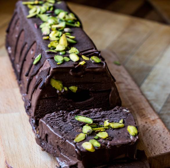 Dunkles Schokoladen-Semifreddo aus der Kastenform mit Pistazien getoppt angeschnitten auf einem Holzbrett