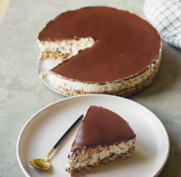 Stracciatella Torte ohne Backen angeschnitten auf einer Kuchenplatte, davor ein Stück auf einem Kuchenteller
